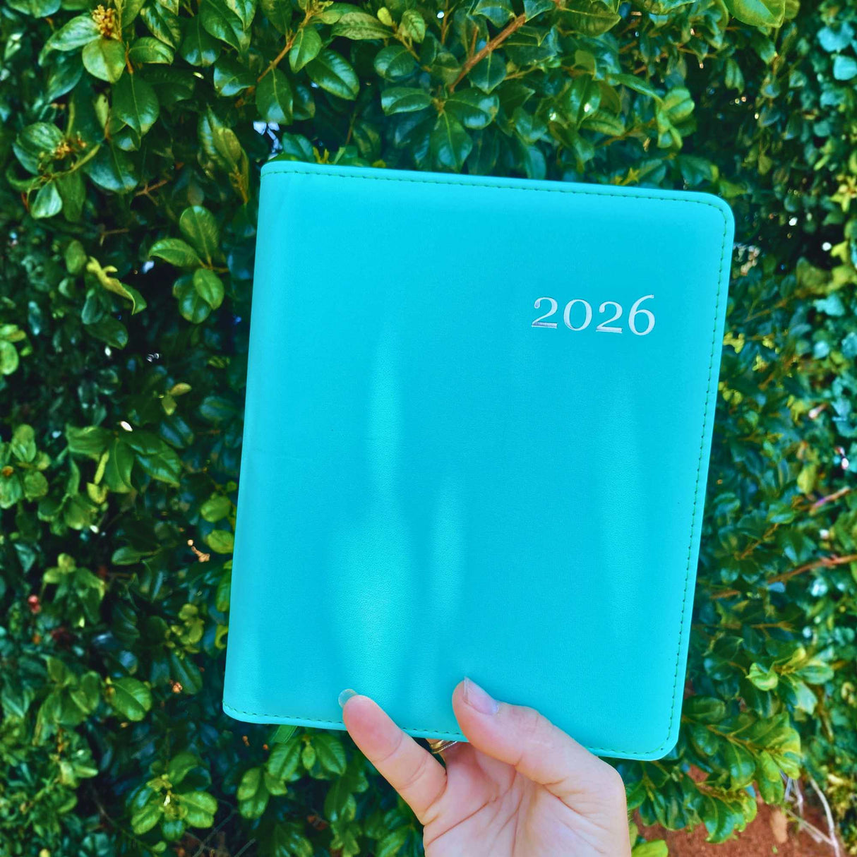Front cover of aqua blue 2026 hardcover planner held in hand