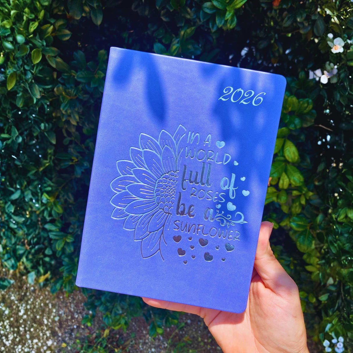 Close-up of 2026 diary with blue sunflower cover – In a world full of roses, be a sunflower
