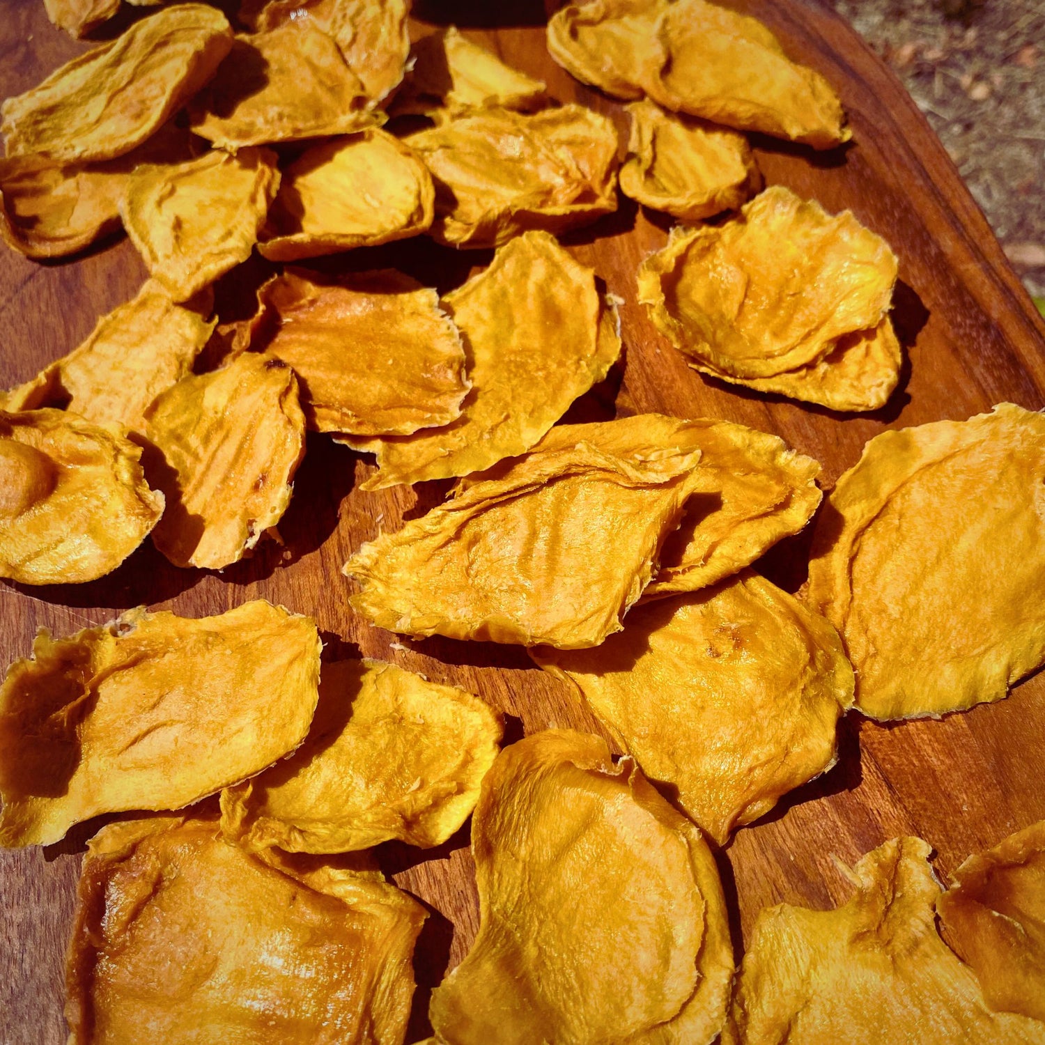 Close-up of biteβsized dried mango minis scattered across a wooden board, showing their naturally varied shapes and chewy texture.