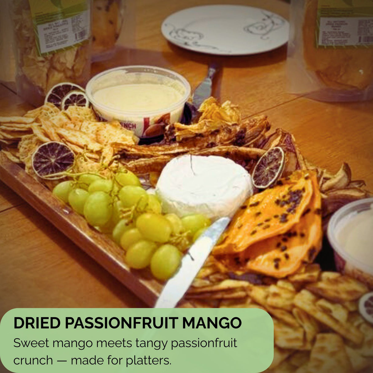 Slices of dried mango with passionfruit seeds featured on a wooden grazing board alongside grapes, cheese, dips, and crackers — ideal as a platter addition.