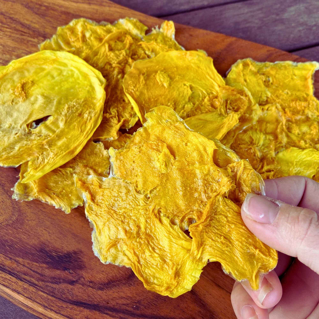 Hand holding multiple slices of Standard Australian dried mango showing natural colour and thickness variation.