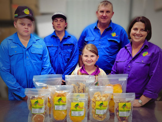 The Tropical Harvest family in North Queensland standing behind their Australian dried fruit packs, including mango, pineapple, and banana.