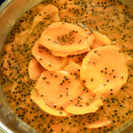 Australian dried mango slices dipped in fresh passionfruit pulp during mango passionfruit preparation.