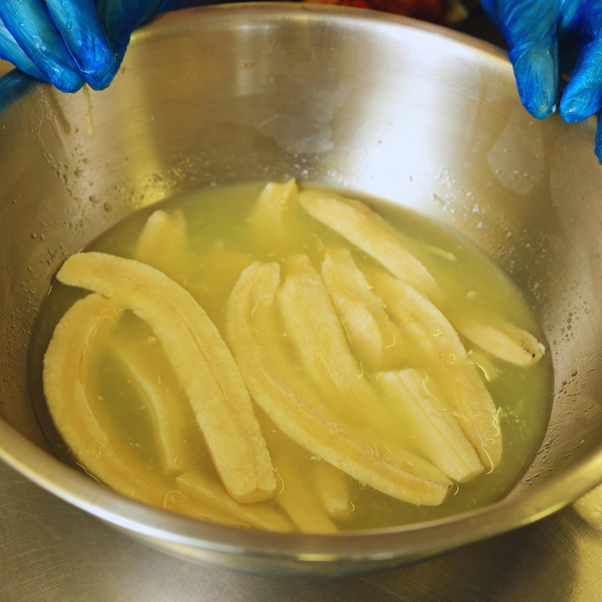 Banana slices soaking in lime juice before drying, showing the natural process that creates the citrus flavour in dried banana with lime