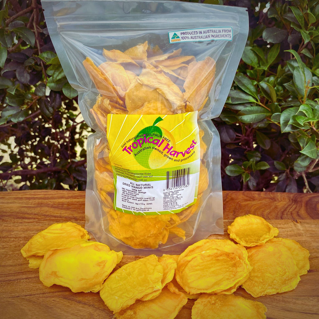 500g resealable pack of dried mango minis with visible label, displayed behind loose dried mango slices on a wooden surface. Highlights packaging details, individual slice size, and sulphur-free, Australian-grown ingredients.