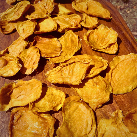 Close-up of bite‑sized dried mango minis scattered across a wooden board, showing their naturally varied shapes and chewy texture.