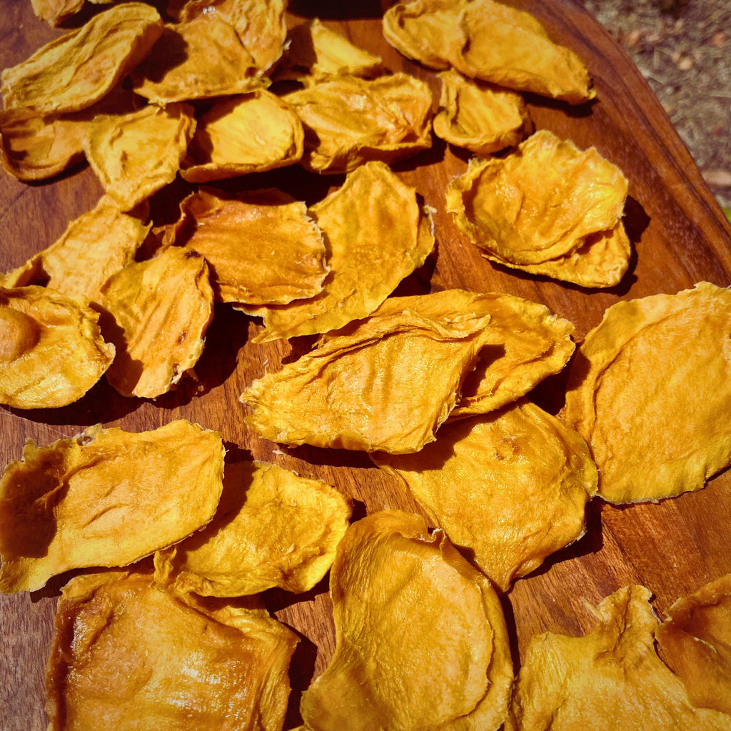 Close-up of bite‑sized dried mango minis scattered across a wooden board, showing their naturally varied shapes and chewy texture.