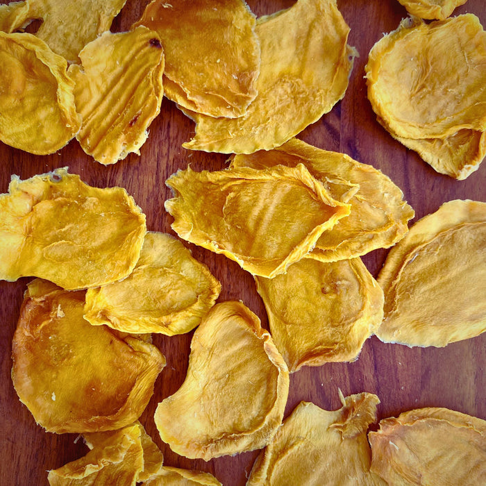 Top-down view of several dried mango minis on a wooden surface, highlighting their firm, chewy texture and golden-orange colour.