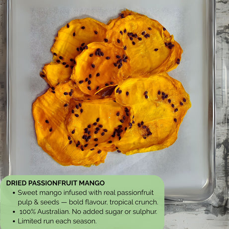 Detailed view of dried passionfruit mango slices on parchment-lined tray, showing glossy dried mango flesh with visible passionfruit seeds. Text overlay reads: ‘Sweet mango infused with real passionfruit pulp & seeds — bold flavour, tropical crunch. 100% Australian. No added sugar or sulphur. Limited run each season.