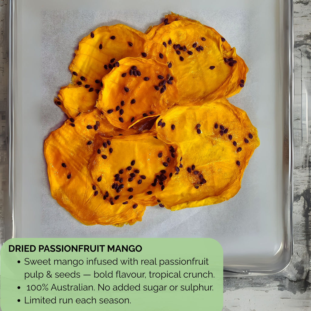 Detailed view of dried passionfruit mango slices on parchment-lined tray, showing glossy dried mango flesh with visible passionfruit seeds. Text overlay reads: ‘Sweet mango infused with real passionfruit pulp & seeds — bold flavour, tropical crunch. 100% Australian. No added sugar or sulphur. Limited run each season.