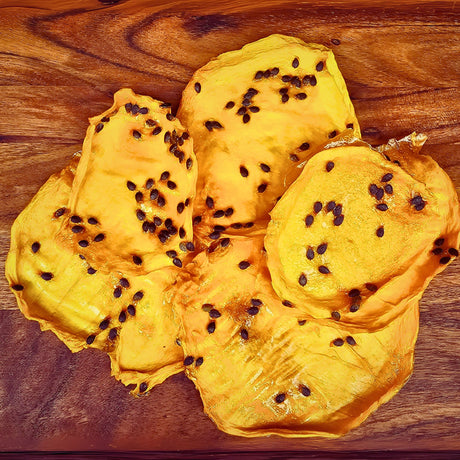 Close-up of dried mango fruit slices infused with passionfruit seeds, displayed on a wooden board to show chewy texture and natural dried finish.