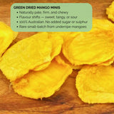Green Dried Mango Minis on wooden surface with overlay text describing product highlights: pale, firm, chewy texture and varying flavour.