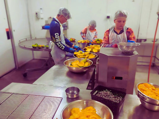 Team members hand-preparing mangoes for drying at Tropical Harvest's food facility in Queensland, Australia