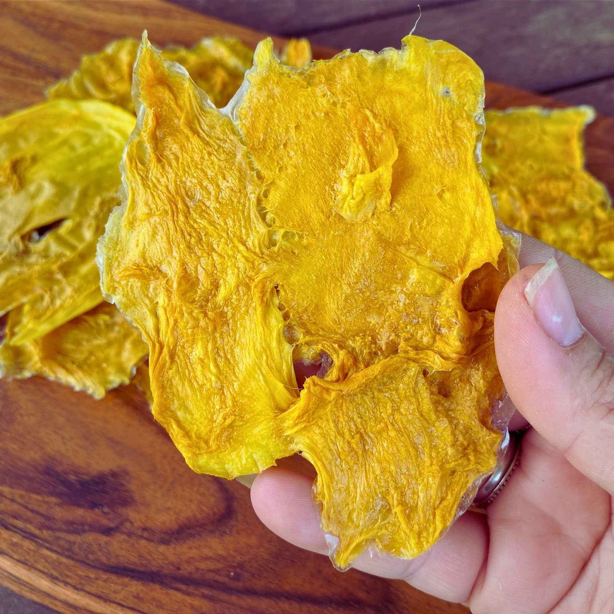Close-up of a large slice of Standard Australian dried mango held in hand, highlighting natural texture and grading variation.