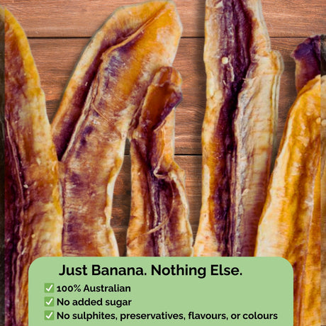 Dried banana long slices on a wooden background with text overlay: "Just Banana. Nothing Else." No sugar, no sulphites, no preservatives.