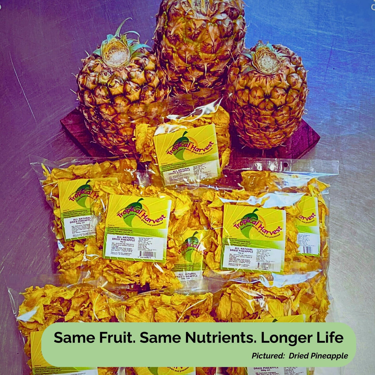 Display of fresh pineapples alongside multiple Tropical Harvest dried pineapple packs. Text overlay: "Same Fruit. Same Nutrients. Longer Life."